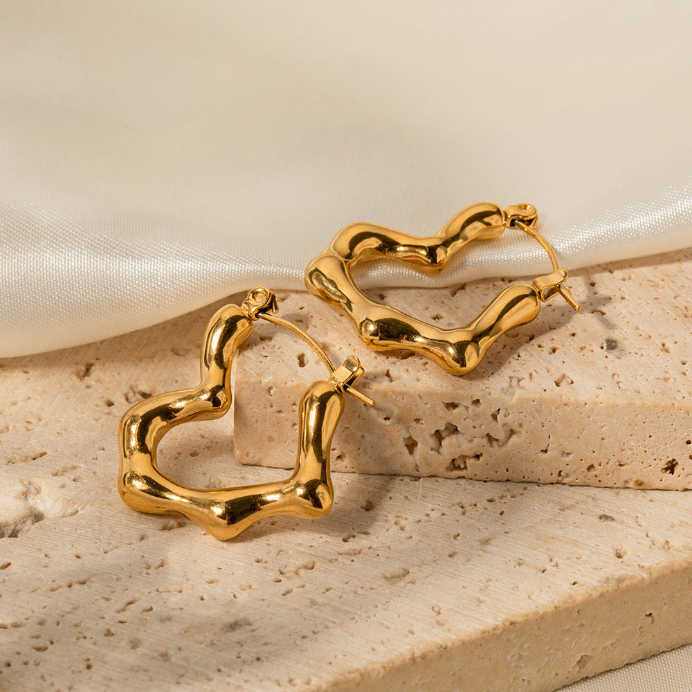 Gold hoop earrings on a beige stone surface with a soft fabric background