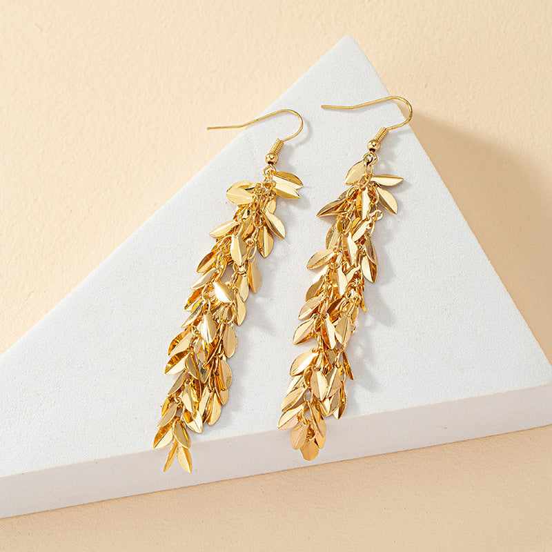 Gold leaf earrings on a white triangle with beige background