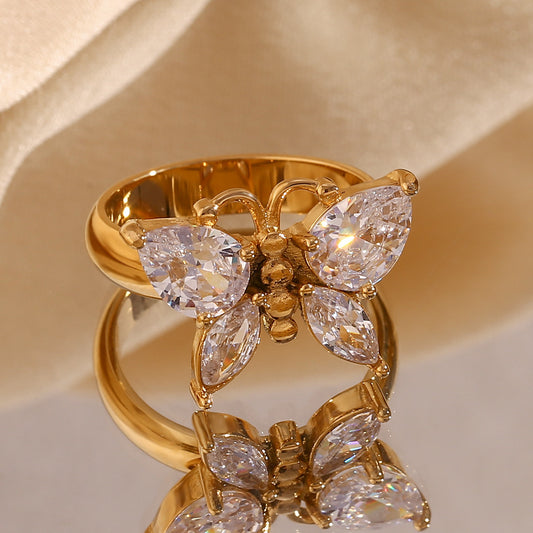Gold ring with butterfly design and clear gemstones on a beige background