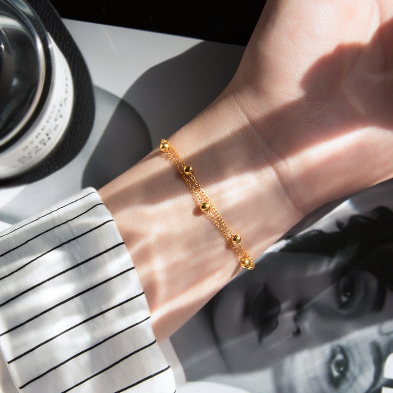 Gold beaded necklace with delicate chain, styled draped over a white coral-like sculpture.