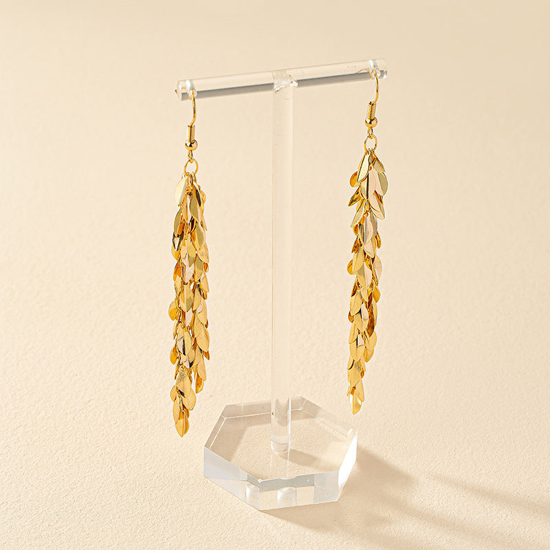 Gold leaf earrings on a clear stand against a beige background