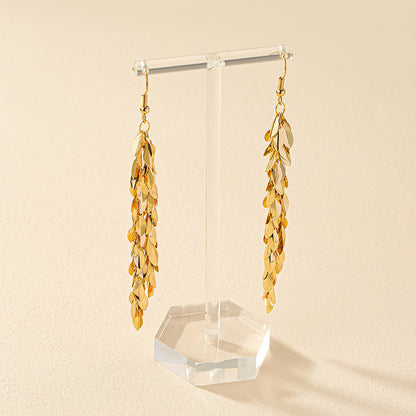 Gold leaf earrings on a clear stand against a beige background