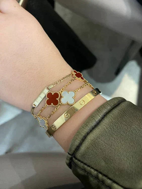 Close‑up of layered gold bracelets: clover motifs, chain links, heart pendant on soft background.