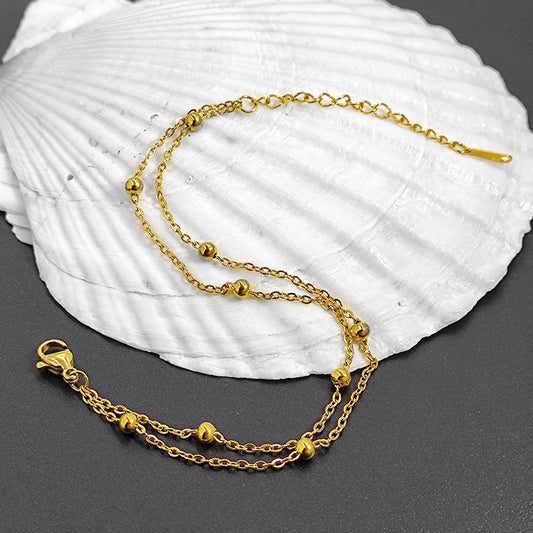 Gold layered chain bracelet elegantly draped over a white seashell.