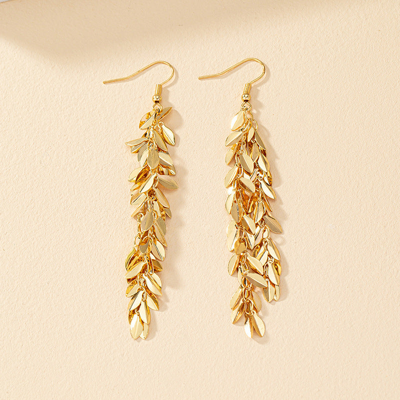 Gold leaf-shaped earrings on a beige background