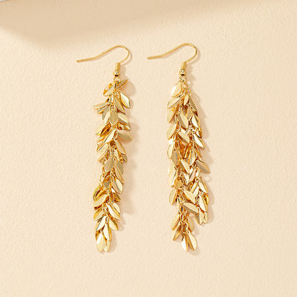 Gold leaf-shaped earrings on a beige background