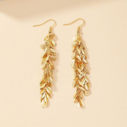 Gold leaf-shaped earrings on a beige background