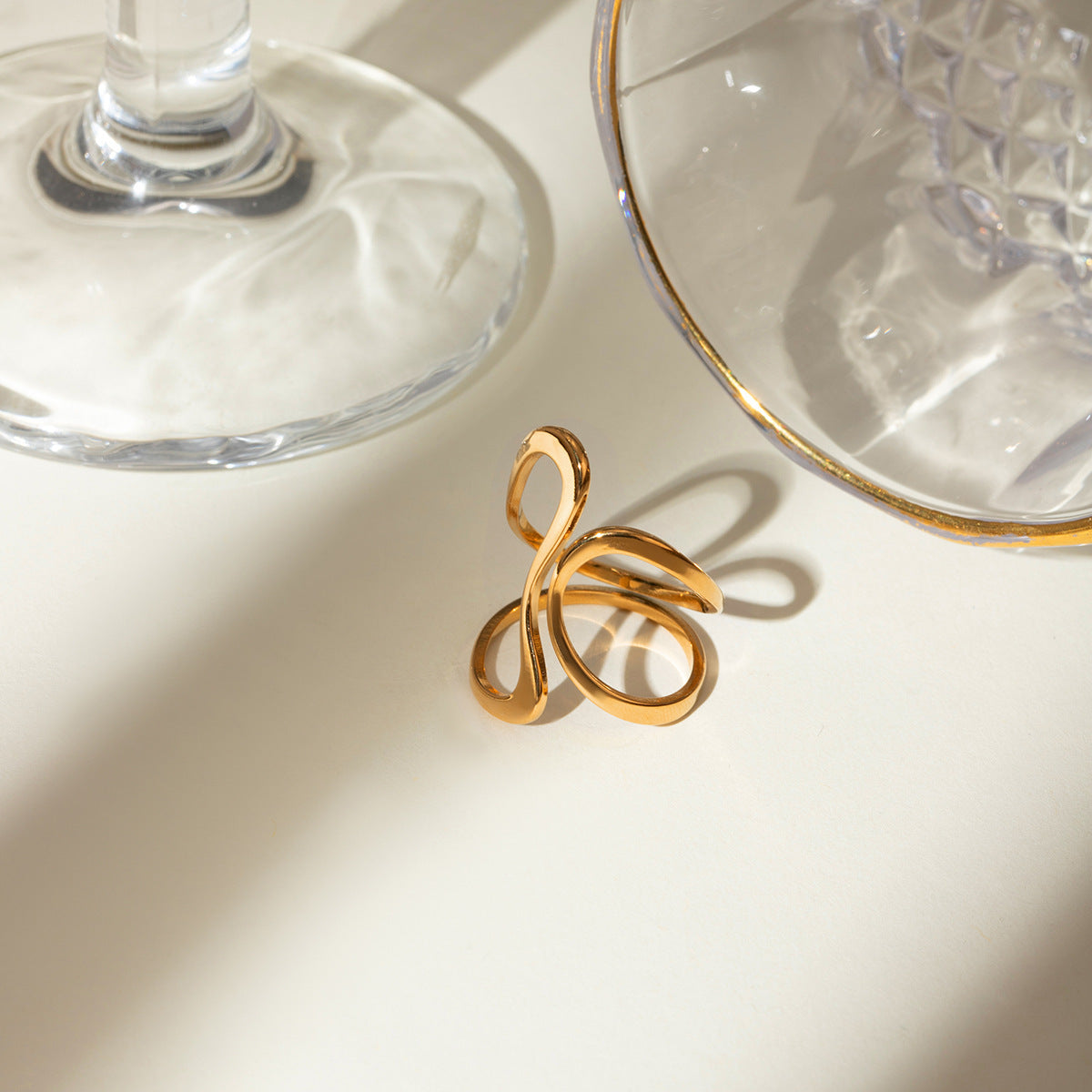 Gold ring with a unique design on a light surface with glassware in the background