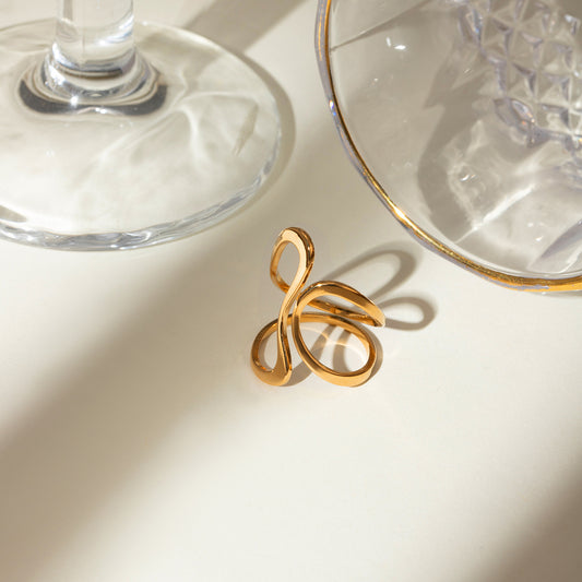 Gold ring with a unique design on a light surface with glassware in the background