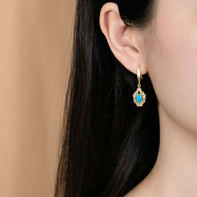 Gold earring with a blue gemstone worn by a model against a beige background
