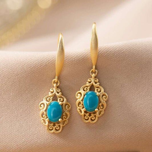 Gold earrings with turquoise stones on a beige fabric background