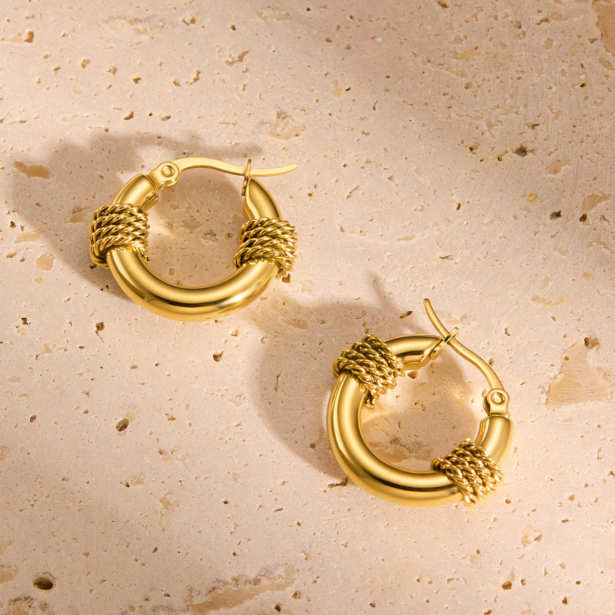 Pair of gold hoop earrings on a beige textured surface