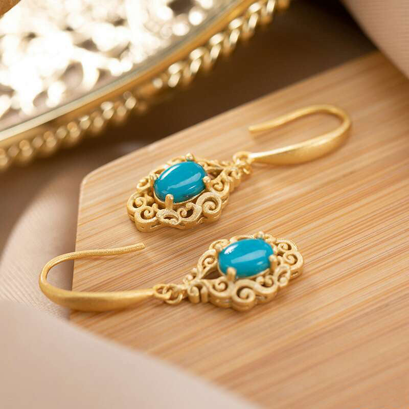 Gold earrings with turquoise stones on a wooden surface