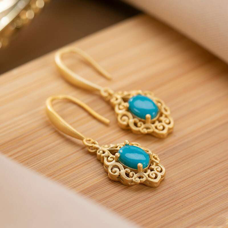Gold earrings with turquoise stones on a wooden surface