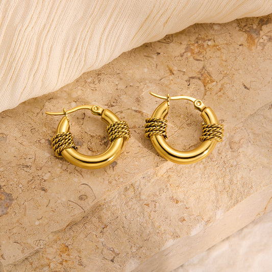 Gold hoop earrings on a textured stone surface