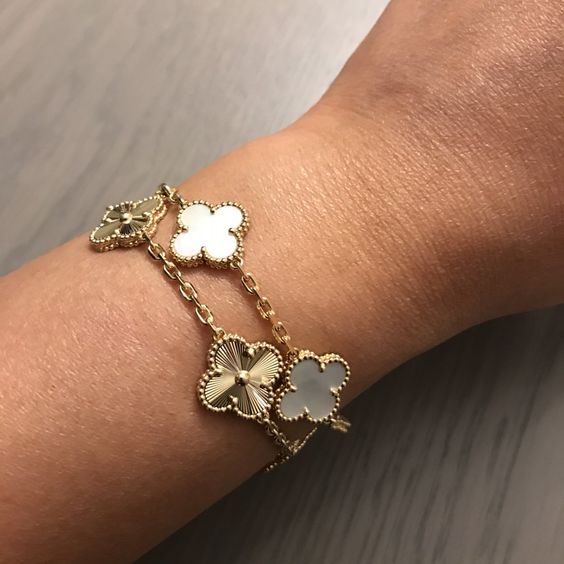 Multiple angles of gold bracelets with clover and heart charms on a light textured surface