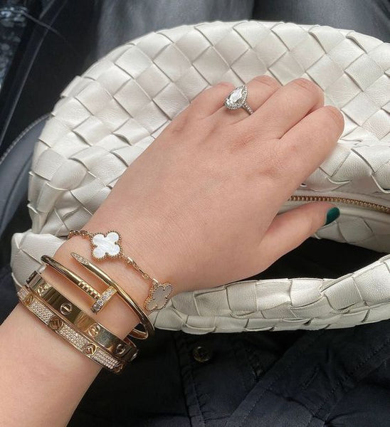 Hand model wearing a gold heart charm bracelet over an olive‑green outfit, styled casually