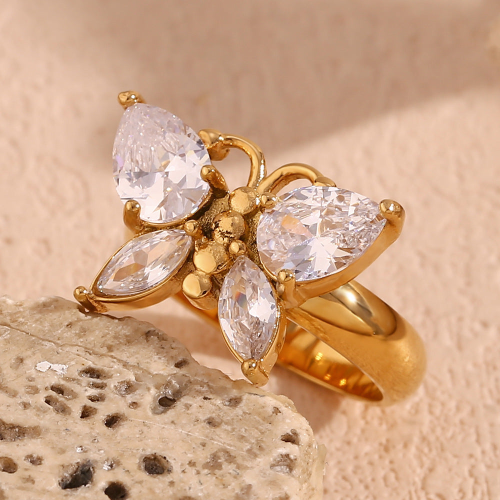 Gold ring with clear gemstones on a textured beige surface
