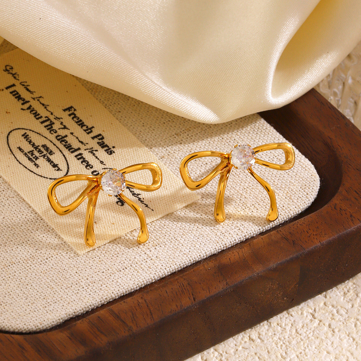Gold bow-shaped earrings with clear stones on a textured surface