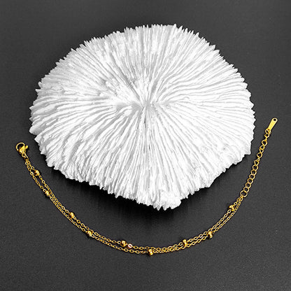 Gold double-chain bracelet with beads, styled on white coral against a dark, textured background