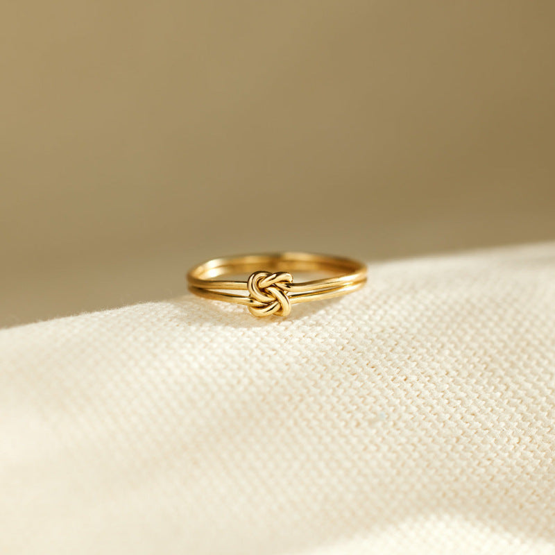 Gold ring with a knot design on a beige fabric background